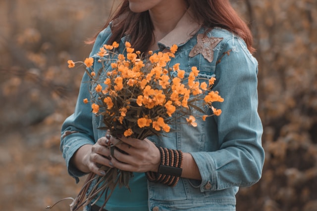 accettare una malattia cronica per rifiorire: in foto una donna con una giacca di jeans e un mazzo di fiori gialli